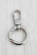 A polished silver metal key ring with a lobster clasp, resting on a light brown wood grain surface.