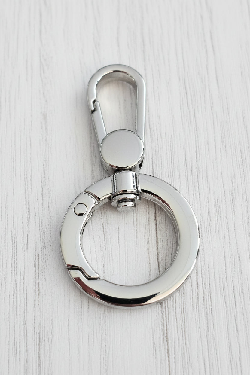 A polished silver metal key ring with a lobster clasp, resting on a light brown wood grain surface.