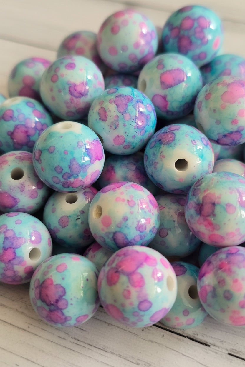 A close-up pile of glossy round beads with a marbled pattern of light blue, pink, and white.