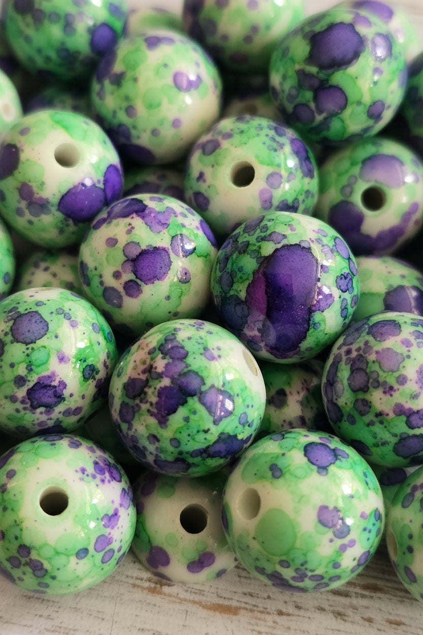 A close-up pile of round beads with a glossy finish, featuring a marbled pattern of vibrant green, purple, and cream.
