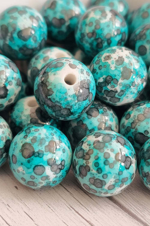 A close-up pile of round turquoise beads with a mottled pattern of black, gray, and white, showing the central hole of each bead.