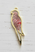 A gold-plated metal bird-shaped pendant or charm with a small hanging loop, filled with dried pink and red flowers