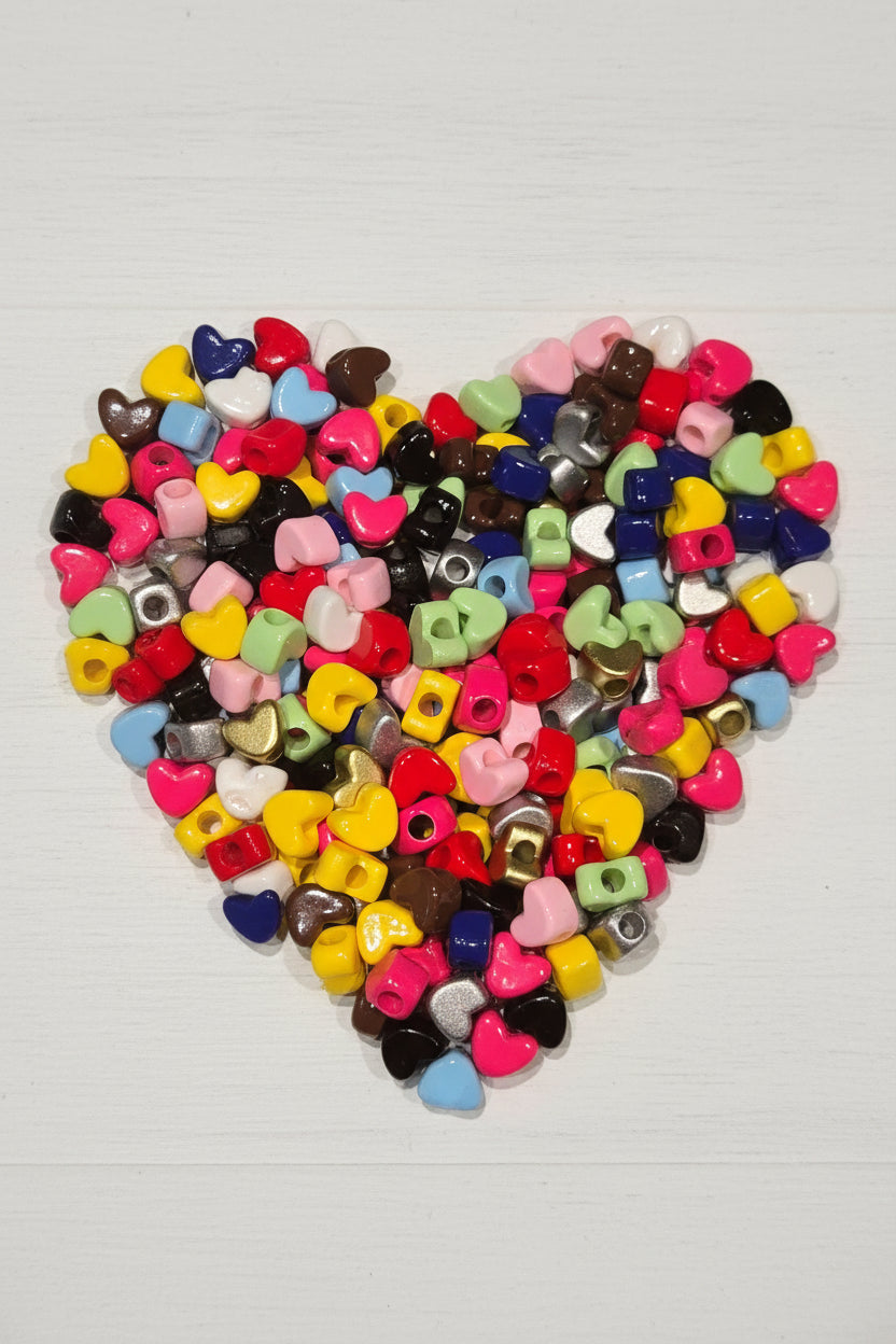 A close-up pile of small glossy heart-shaped beads in multiple colors, including red, pink, yellow, mint green, light blue, black, white, brown, silver, and gold.