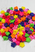 A dense pile of small, glossy, flower-shaped acrylic beads in a vibrant rainbow of colors including pink, red, orange, yellow, green, blue, and purple.