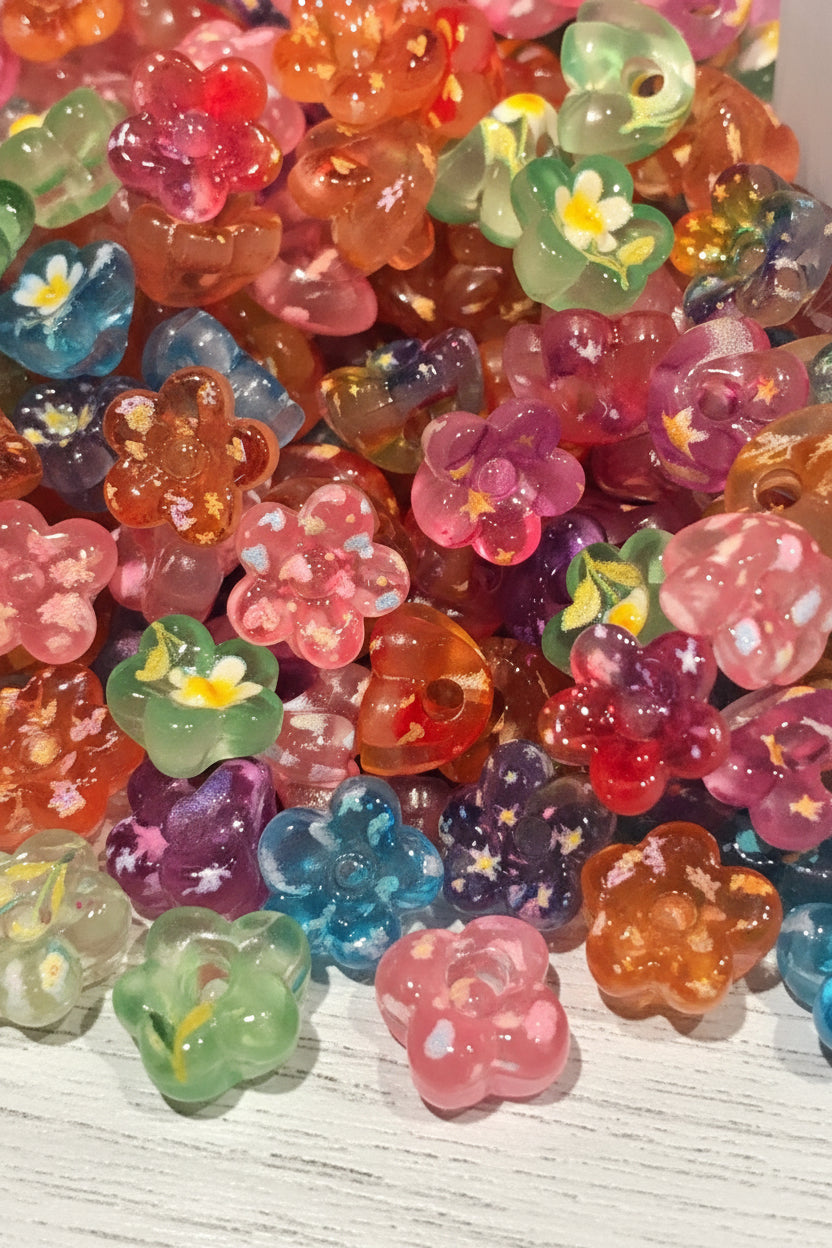 A close-up pile of colorful translucent flower-shaped beads with white and yellow centers, mixed with glitter and swirl patterns in pink, purple, green, orange, and blue.