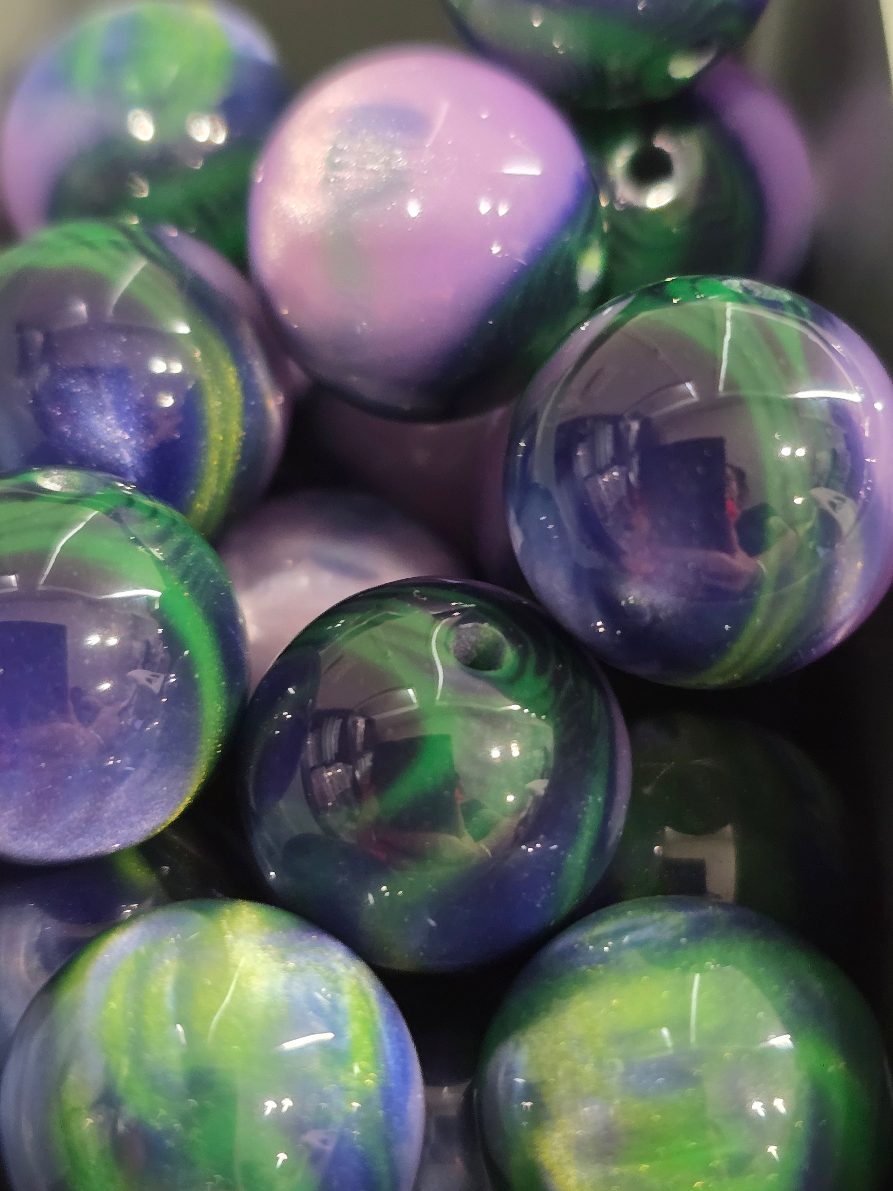 A close-up of glossy marbled glass beads or ornaments in swirls of purple, blue, green, and white.