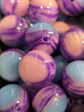 Close-up of glossy round beads with a marbled swirl pattern in purple, light blue, and pale pink.