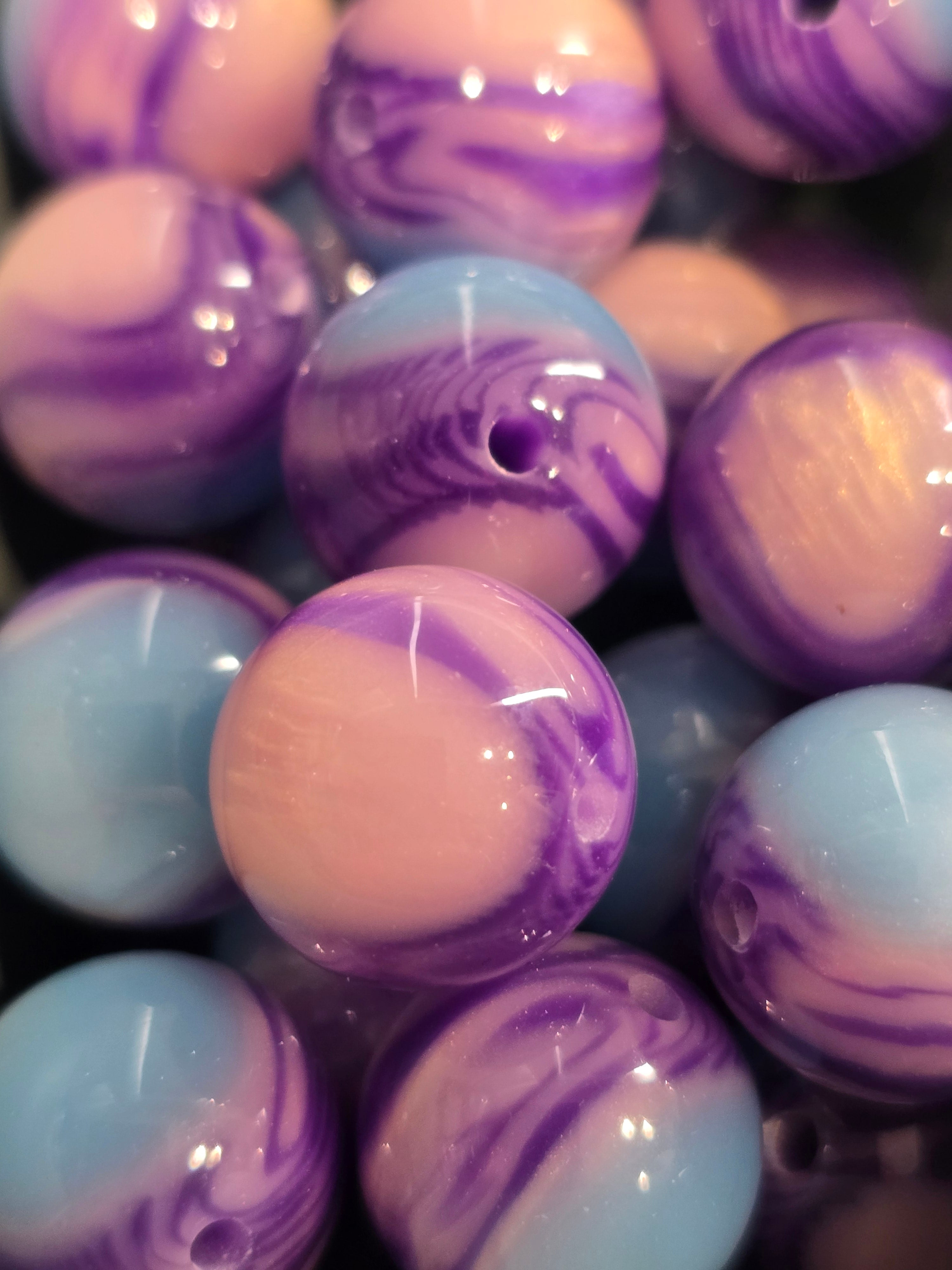 Close-up of glossy round beads with a marbled swirl pattern in purple, light blue, and pale pink.