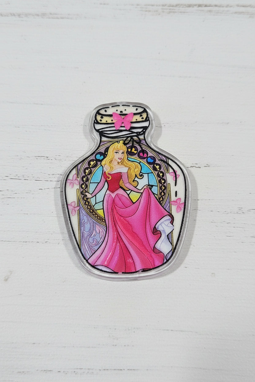 A small illustrated charm or pendant with a glossy finish, featuring a stylized character in a pink dress and gold/yellow hair.