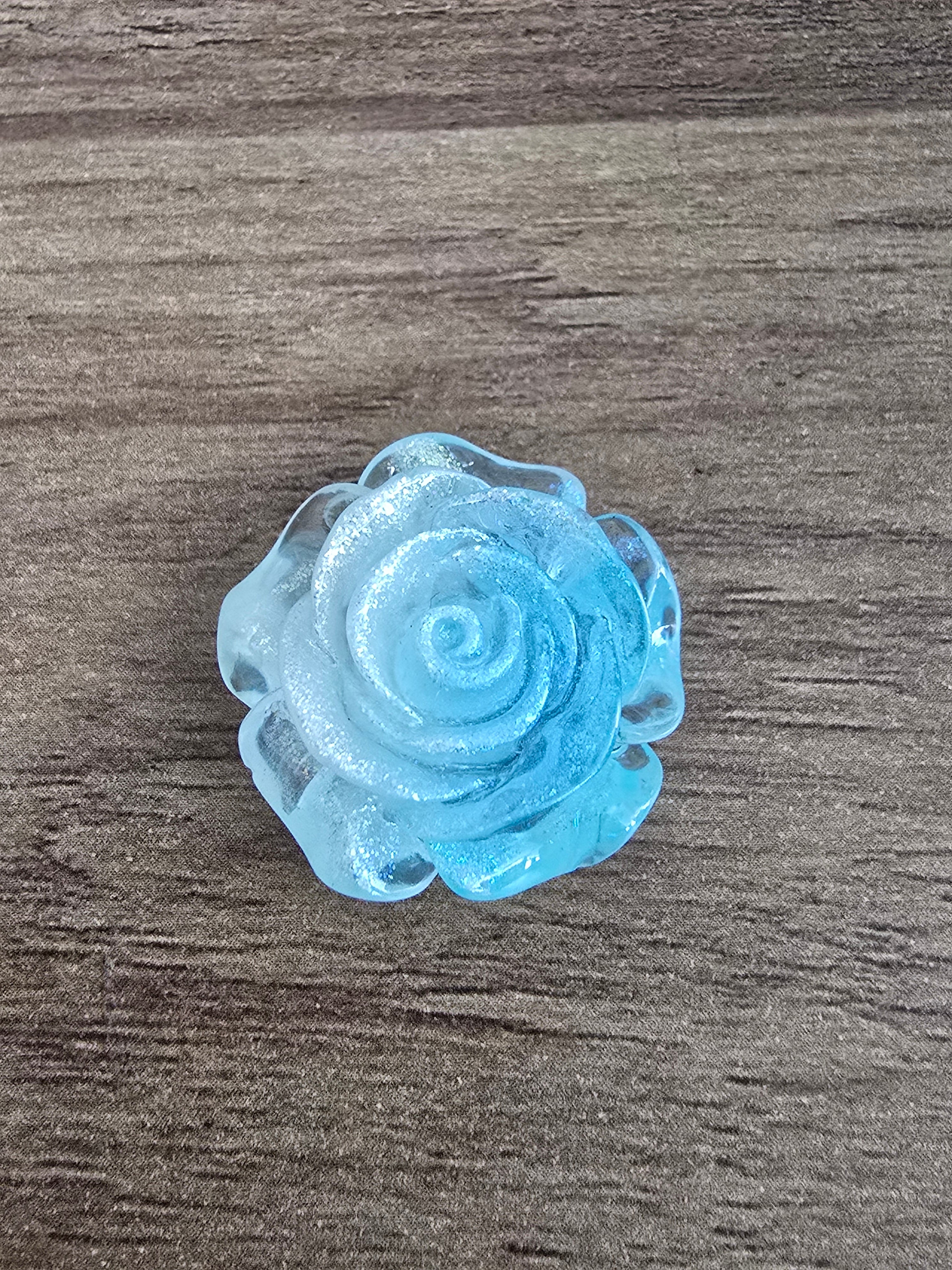 A single blue glittery rose-shaped bead, photographed from above.