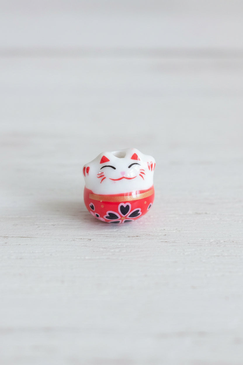 A small decorative bead shaped like a smiling white cat with red and black details.