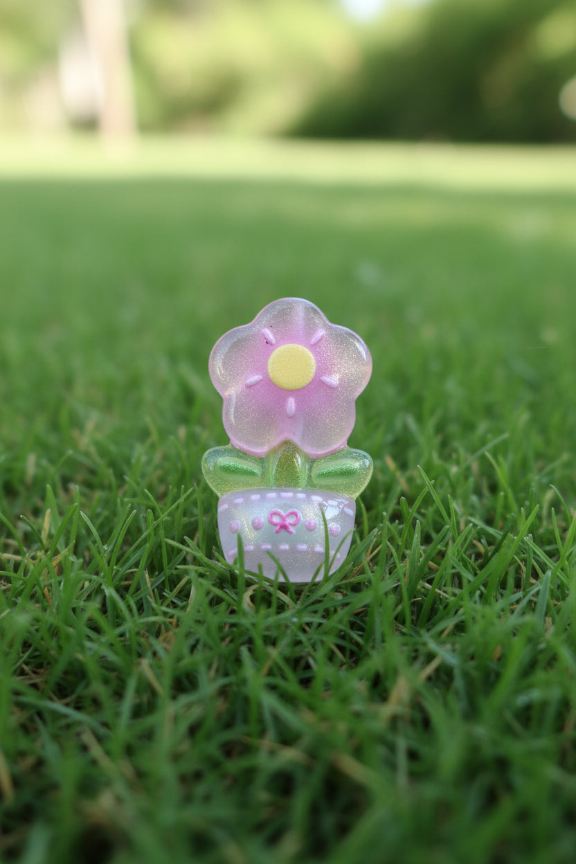A small translucent flower-shaped bead with a yellow center and green stem, standing on a patch of green grass outdoors.