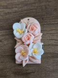 A handmade polymer clay charm featuring pink and white flowers with yellow centers on a light pink rectangular base.