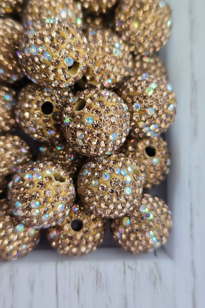 A close-up pile of round, gold-toned beads heavily embellished with small iridescent rhinestones.