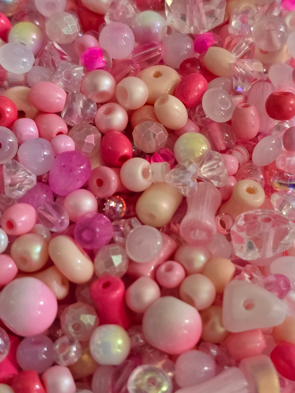 Assorted pink and pastel craft beads, including round glass crystal beads , faceted crystal beads, and cylindrical tubes, in shades of pink, red, and cream.
