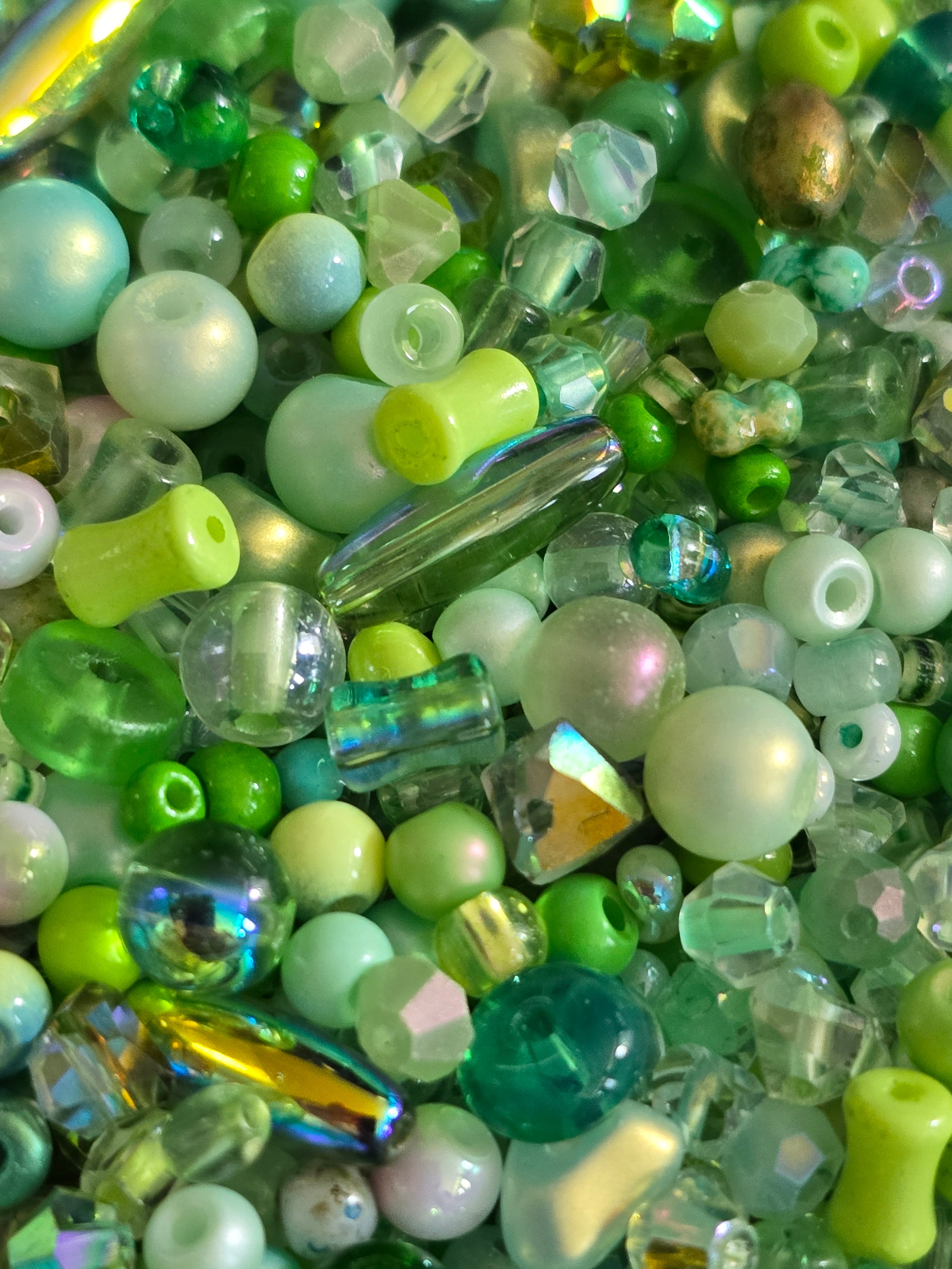 A close-up pile of assorted craft beads in various shapes, sizes, and colors, including light green, mint and iridescent clear beads.