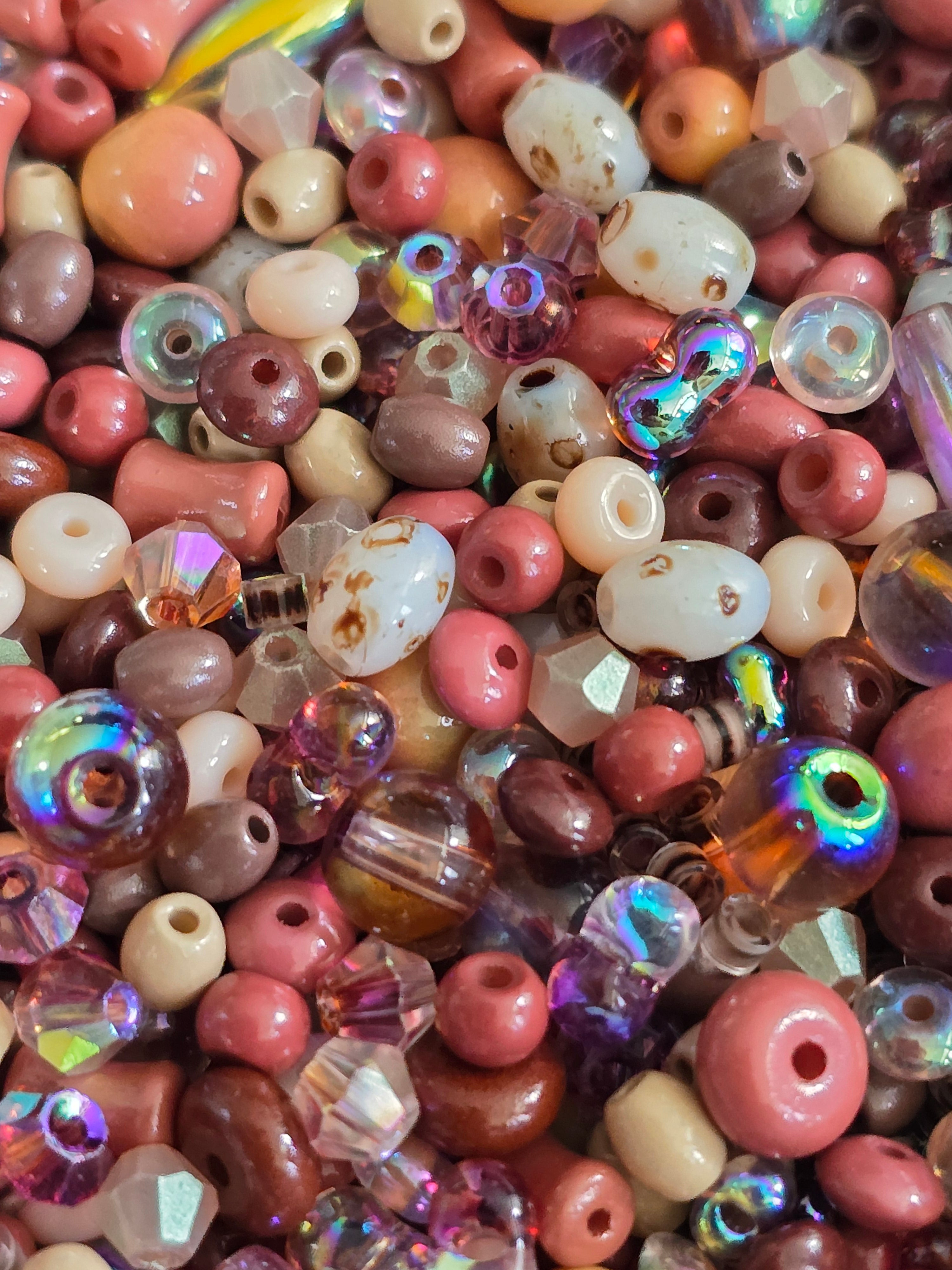 A dense pile of assorted craft beads in various shapes, sizes, and colors, including  cream, brown, and iridescent finishes.