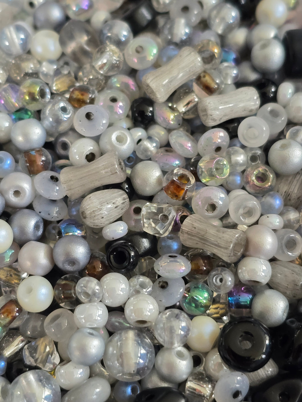 A close-up pile of mixed craft beads in various shapes, sizes, and finishes, including white pearls, clear faceted beads and iridescent pieces.