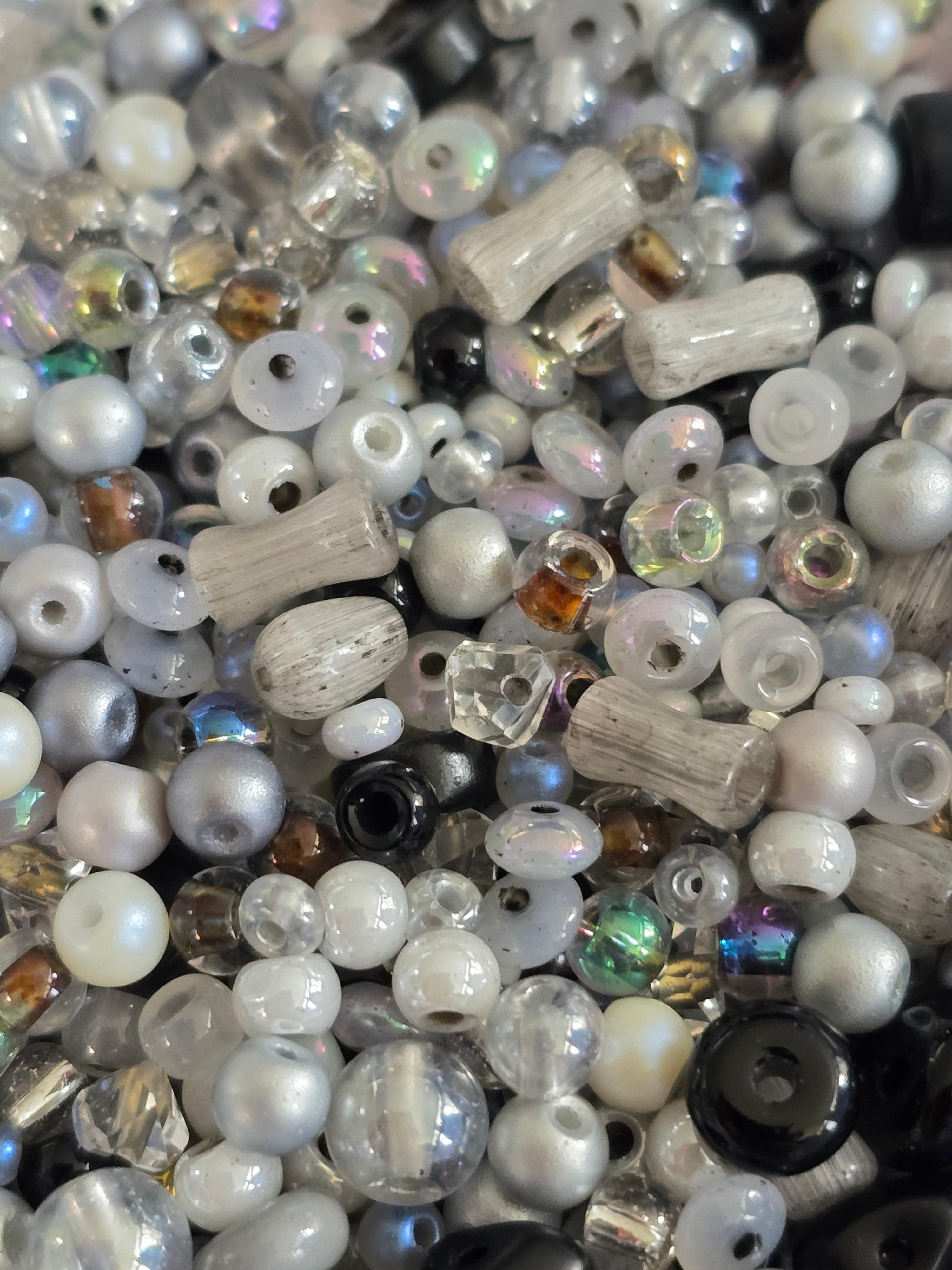 A close-up pile of mixed craft beads in various shapes, sizes, and finishes, including white pearls, clear faceted beads and iridescent pieces.