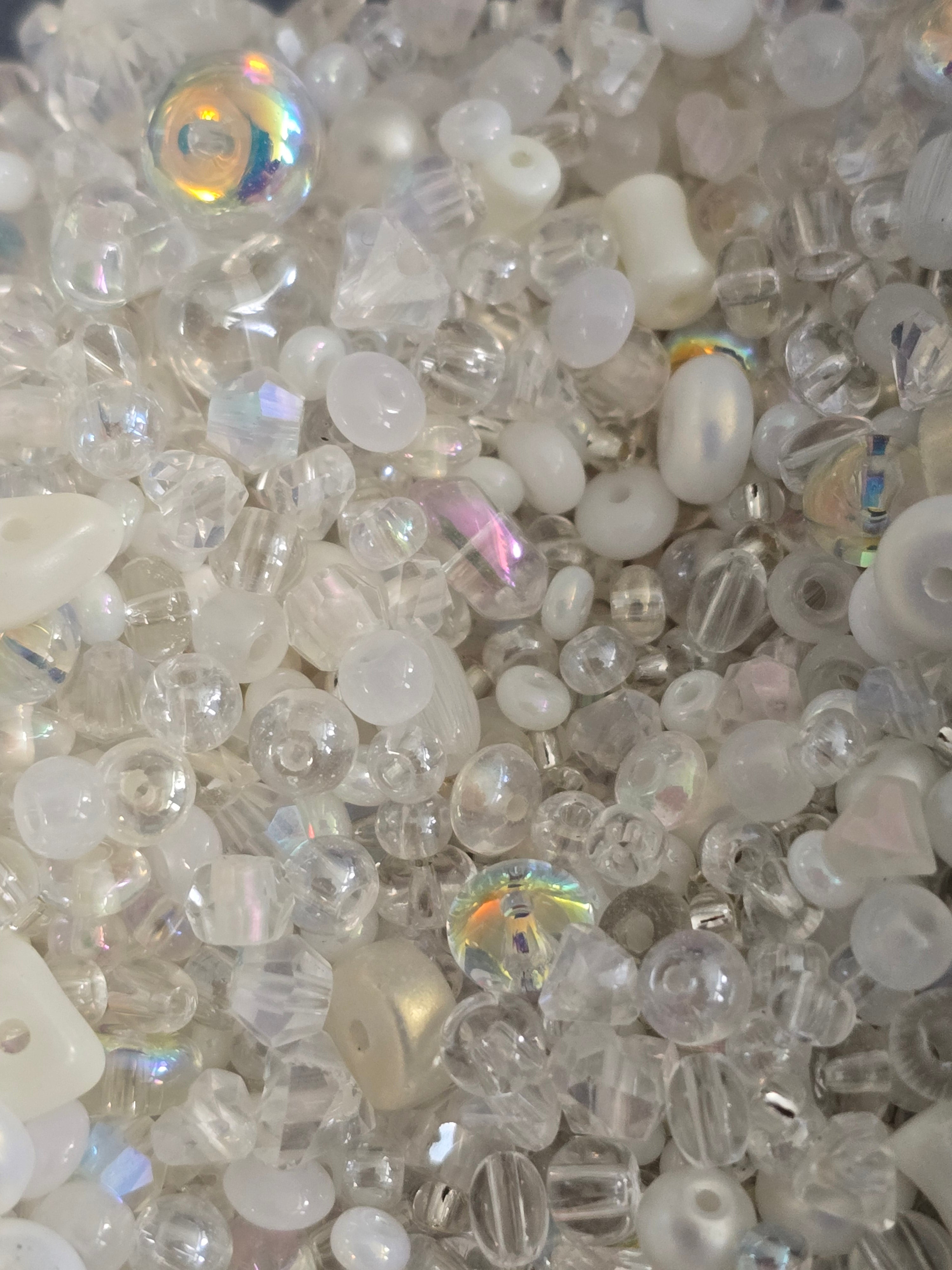 A close-up pile of clear and milky white craft beads with various shapes, including faceted, round, and opaque styles, with a few iridescent accents.