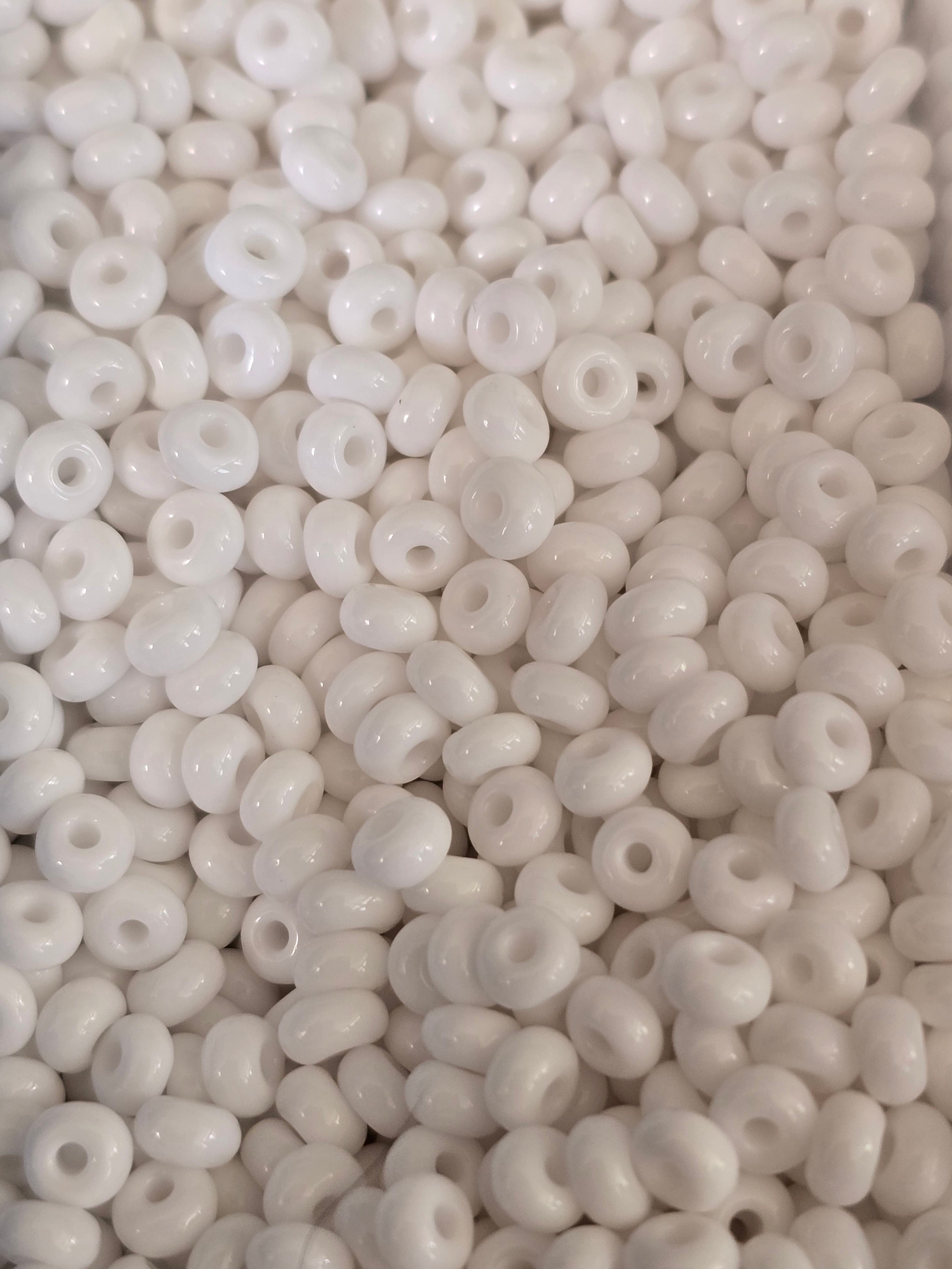 A close-up pile of small, glossy white glass beads with a central hole, filling the entire frame.