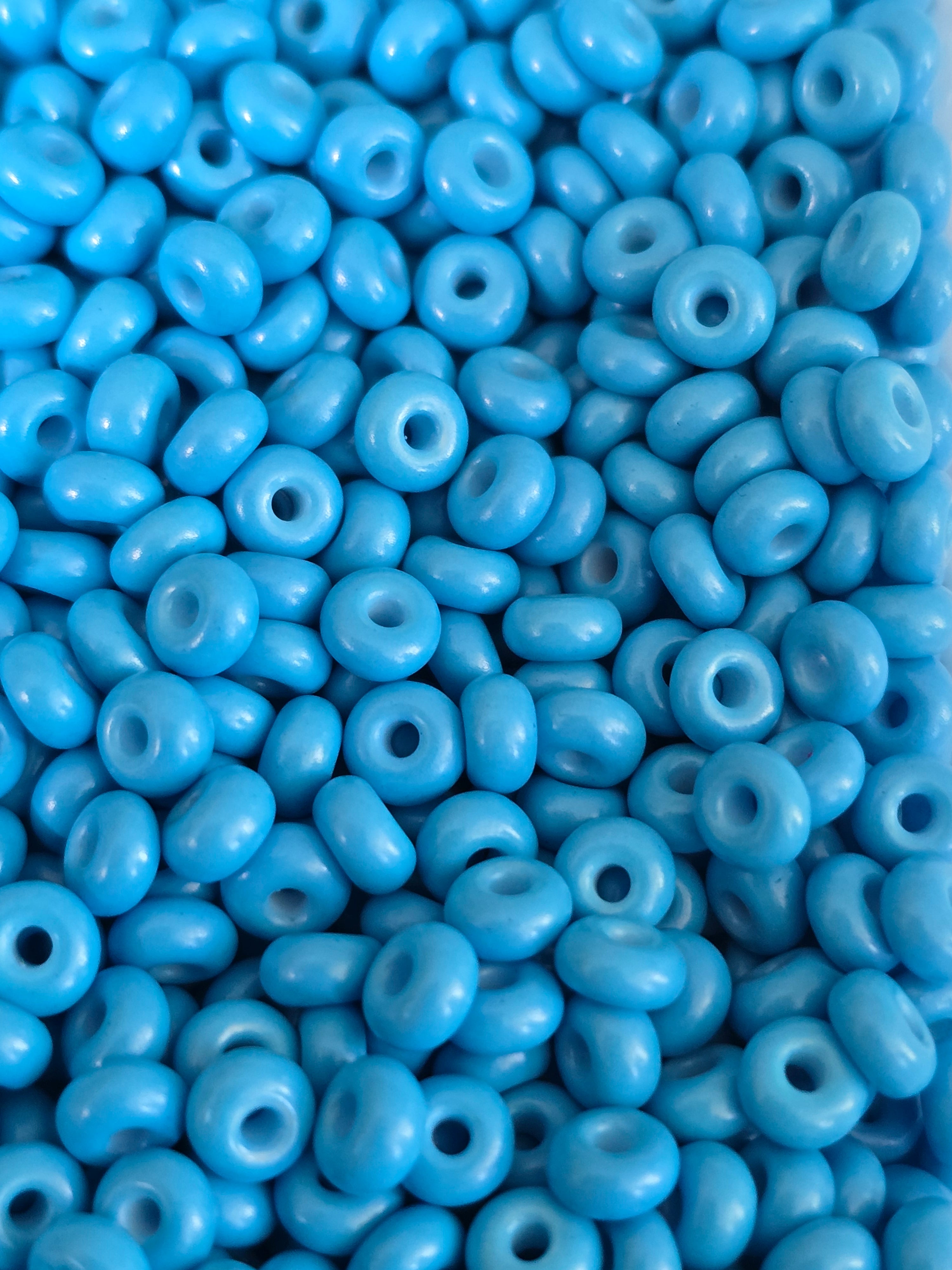 A close-up pile of bright blue round craft beads with central holes, filling the entire frame.
