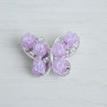 A butterfly-shaped bead featuring light pink roses in a silver-toned filigree frame.
