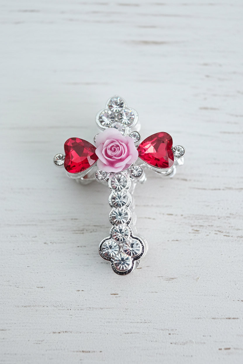 A silver-toned cross-shaped bead featuring a pink rose in the centre, flanked by two red heart-shaped glass crystals.