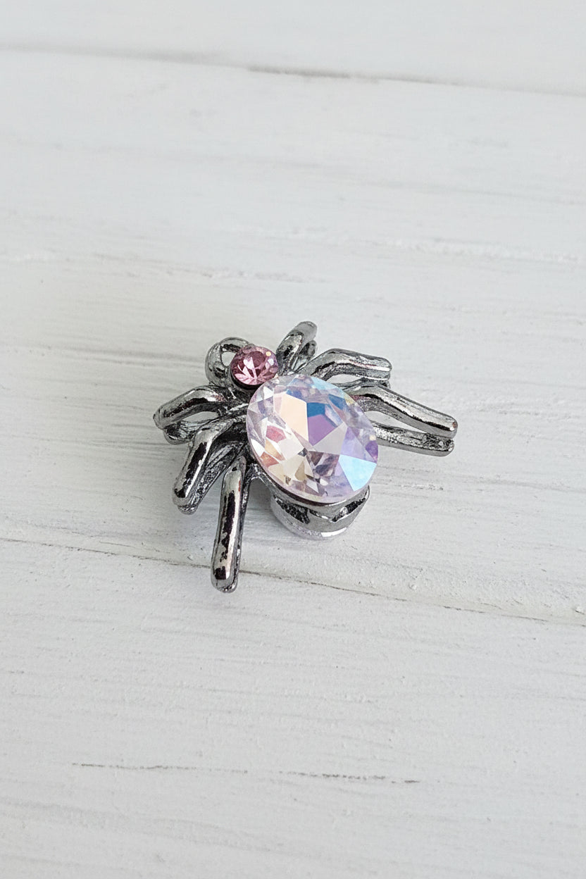 A spider-shaped bead, gunmetal base with a faceted iridescent pink rhinestone body.