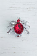 A spider-shaped bead with a faceted red glass crystal body and silver-toned legs