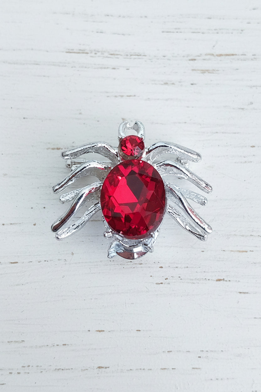 A spider-shaped bead with a faceted red glass crystal body and silver-toned legs