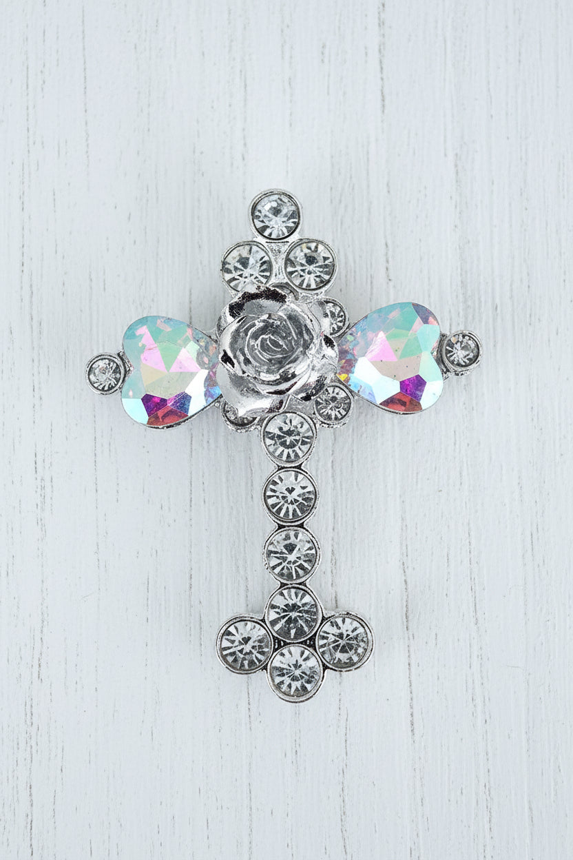 A silver-toned metal cross-shaped bead embellished with clear rhinestones and two faceted iridescent glass crystals showing purple, blue, and green reflections and a silver rose in the centre.