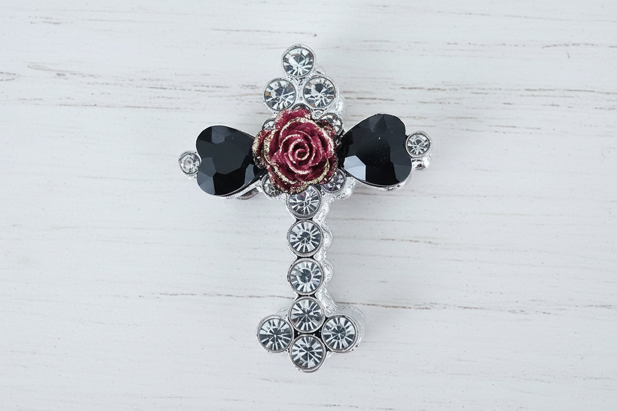 A gothic-style cross bead featuring a central red rose, two faceted black heart-shaped glass crystals, and a halo of clear rhinestones on a silver-toned base.