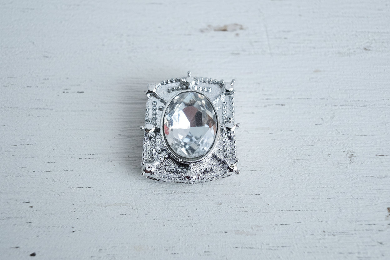 A silver-toned square bead with a large clear oval center stone.