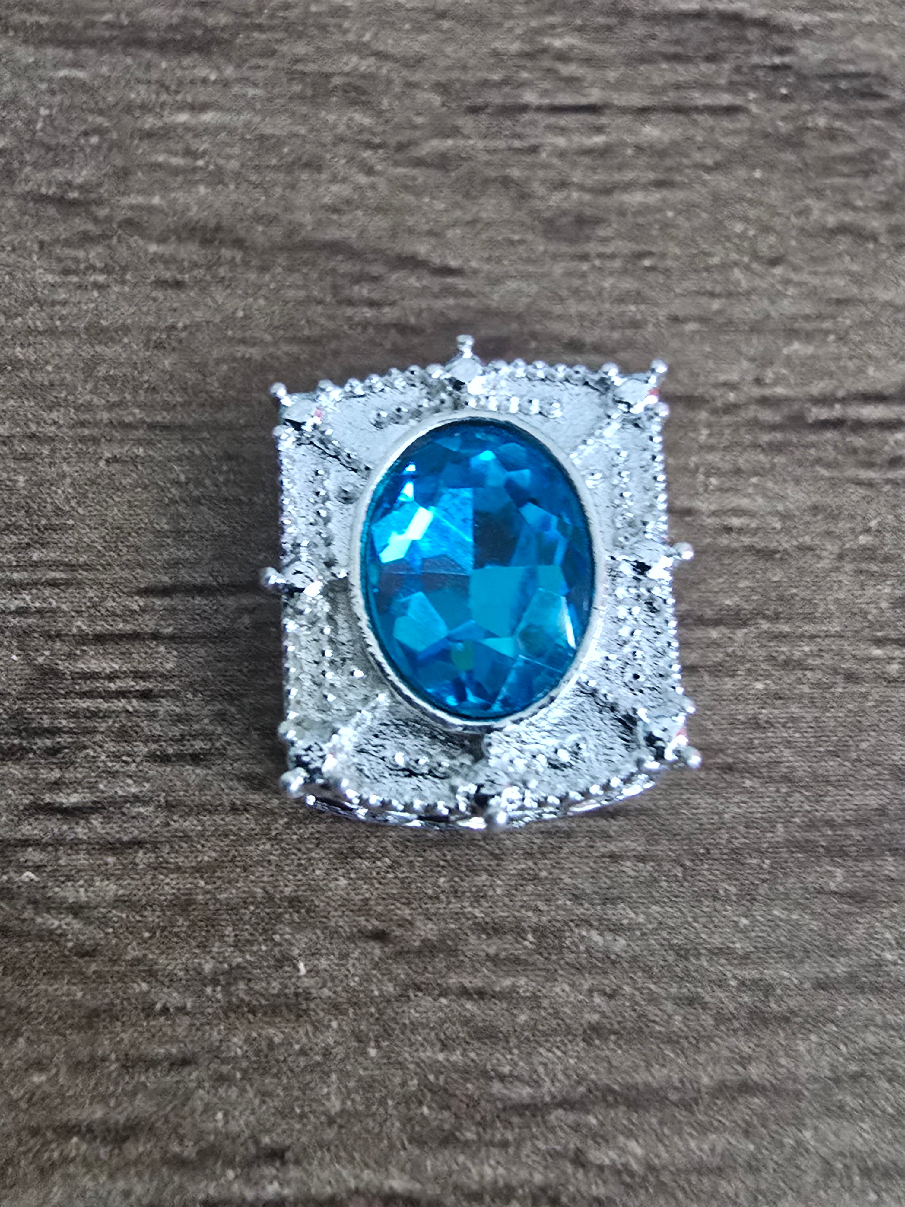 A silver-toned bead featuring an oval-cut blue glass gemstone.