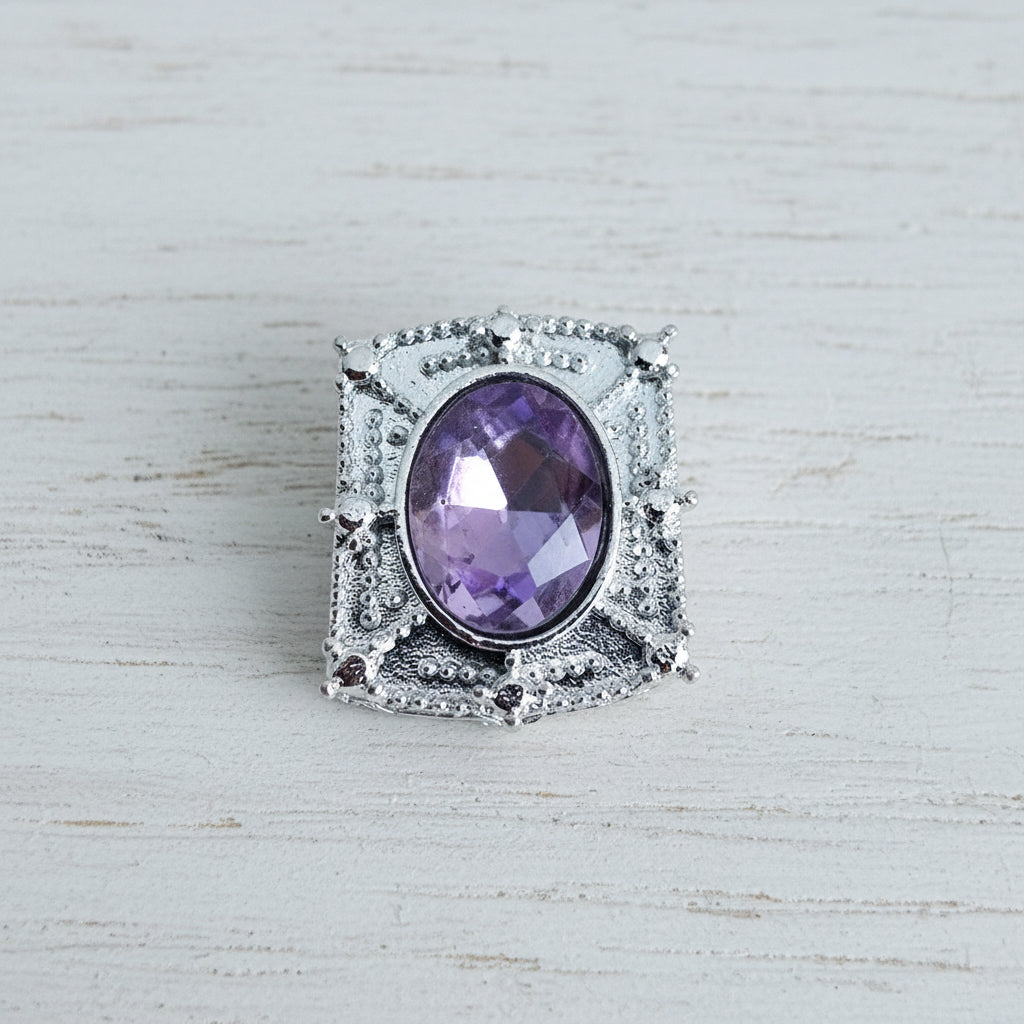 A silver-toned bead featuring an oval-cut purple glass gemstone.
