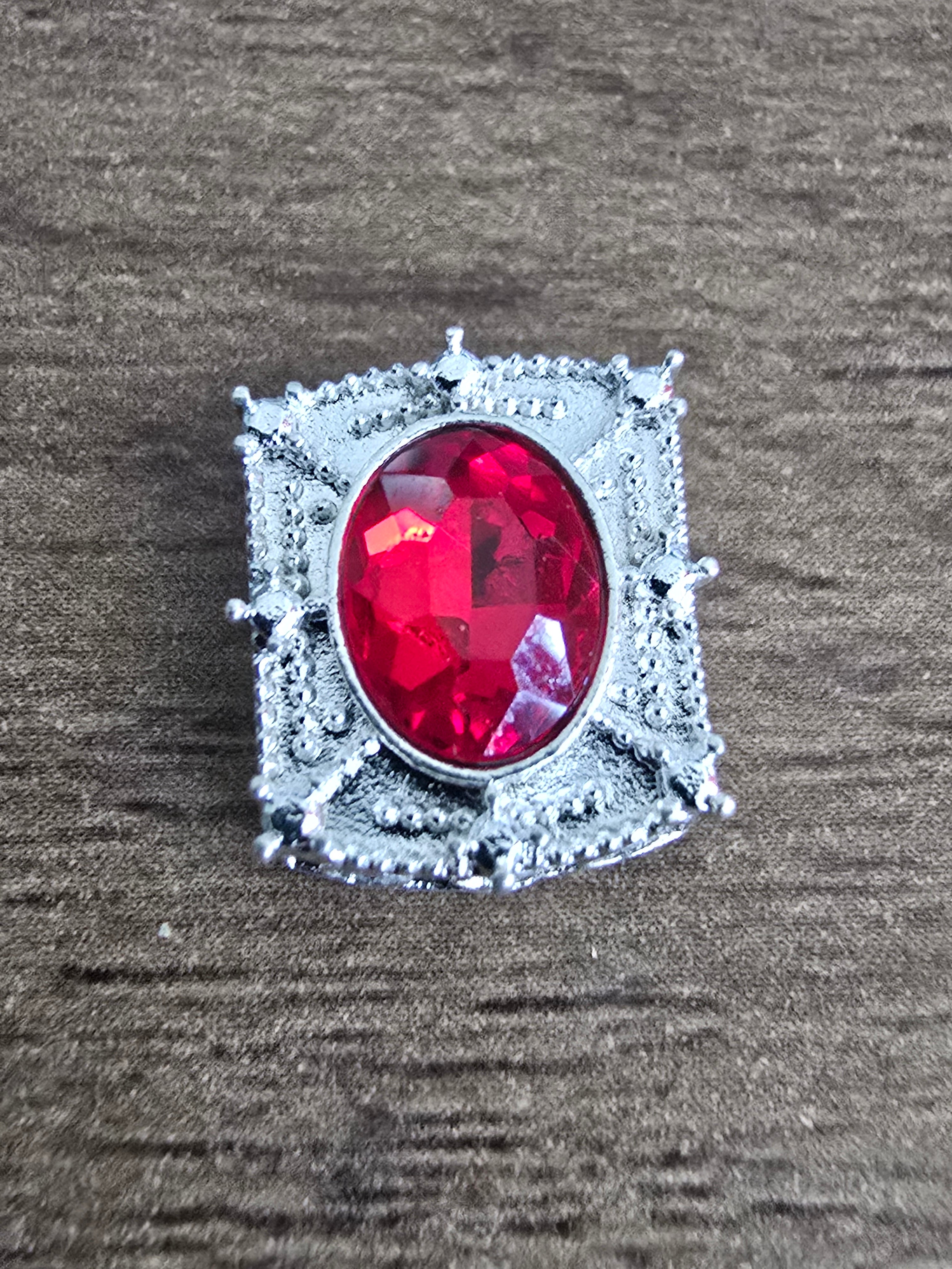 A silver-toned bead featuring a large, oval-cut red gemstone in a decorative, textured setting, displayed on a dark wood surface.
