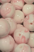 A close-up pile of glossy round beads with a white base and soft pink marbled swirls