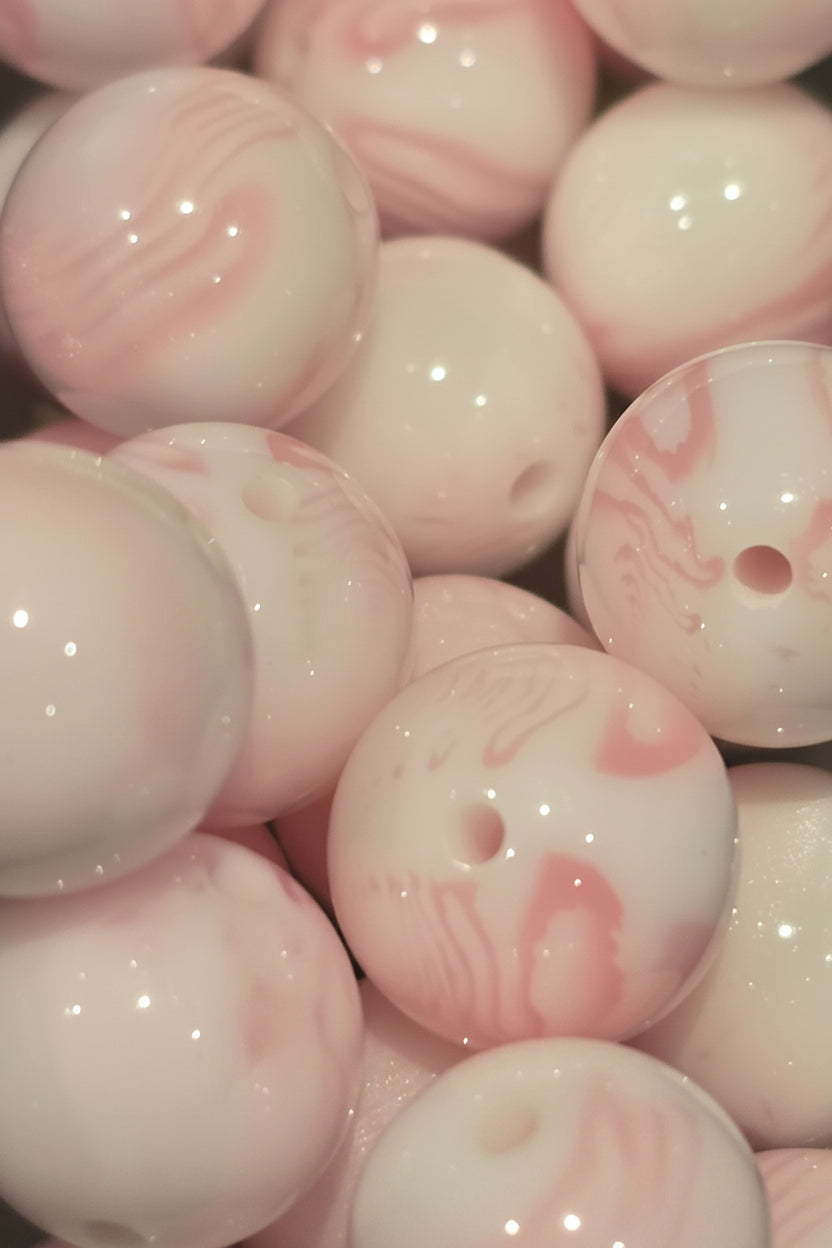 A close-up pile of glossy round beads with a white base and soft pink marbled swirls