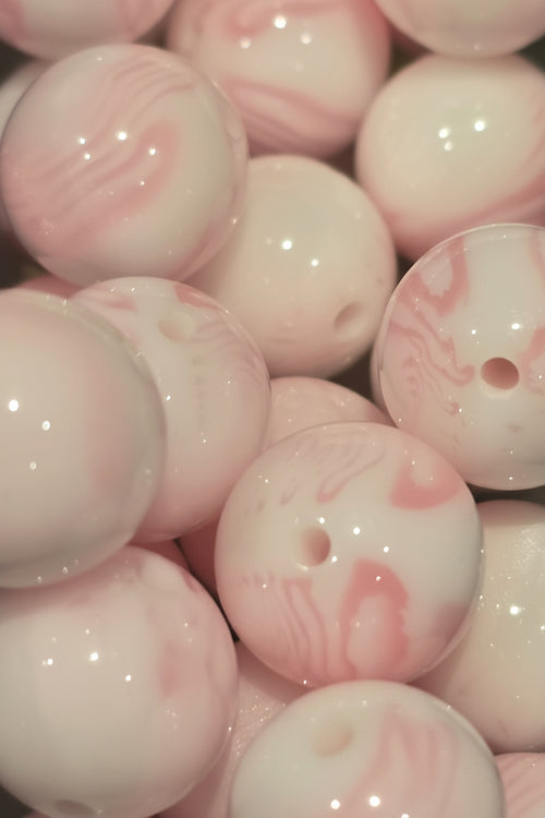 A close-up pile of glossy round beads with a white base and soft pink marbled swirls