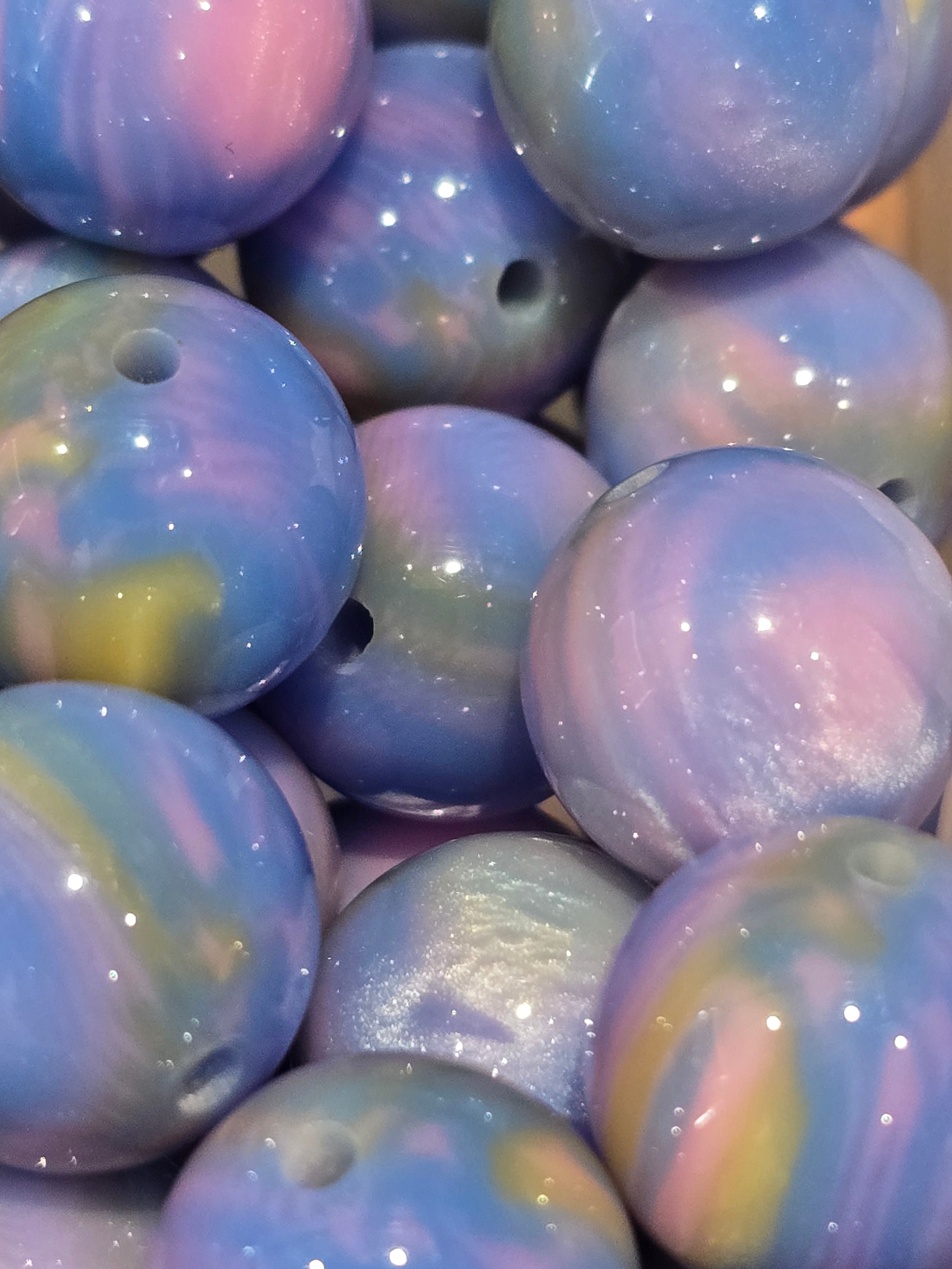 A close-up of glossy, round craft beads with a marbled swirl pattern in pastel shades of blue, purple, pink, and hints of yellow.