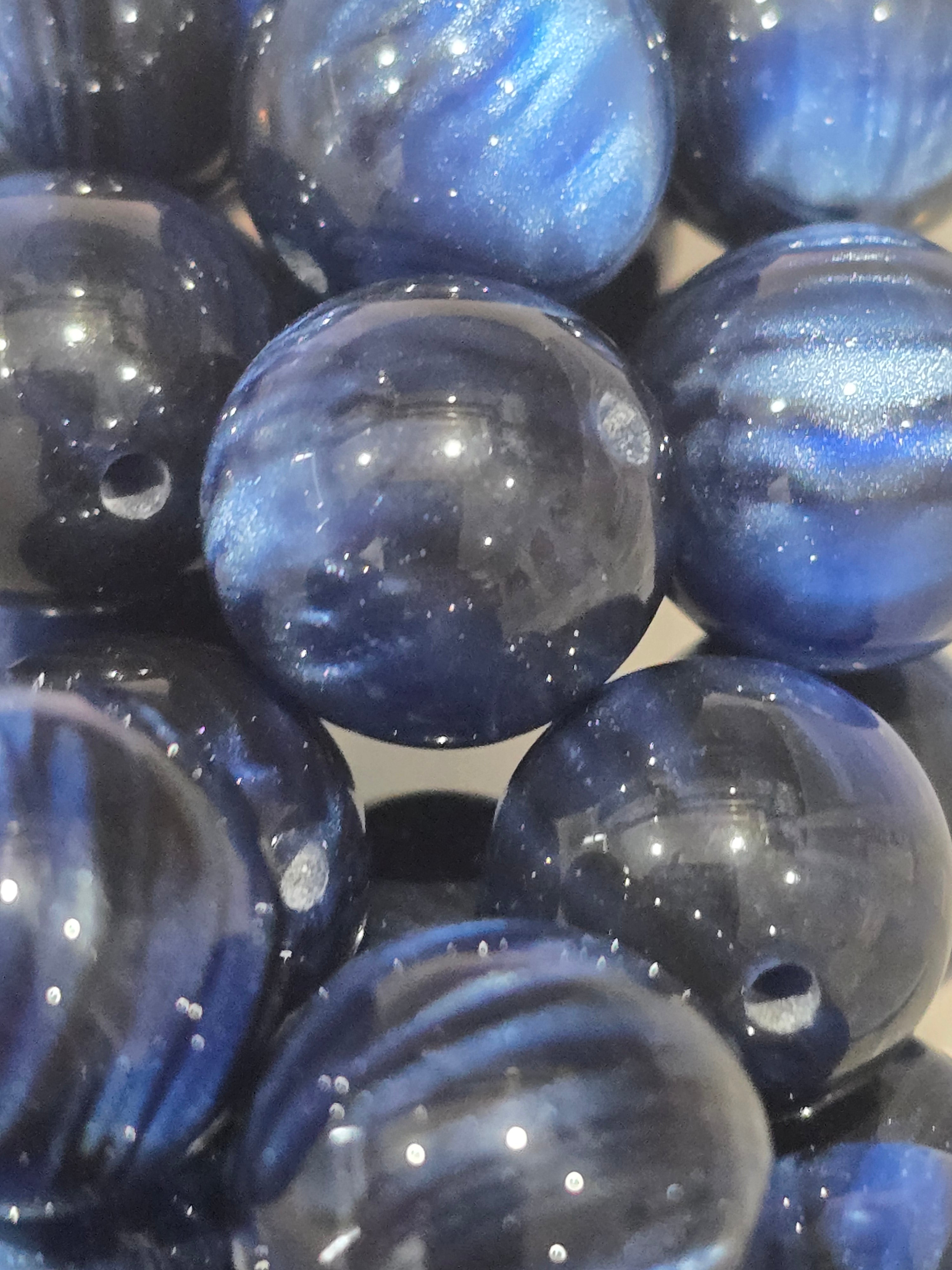 A close-up of glossy, round blue beads with a metallic, starry glitter finish.