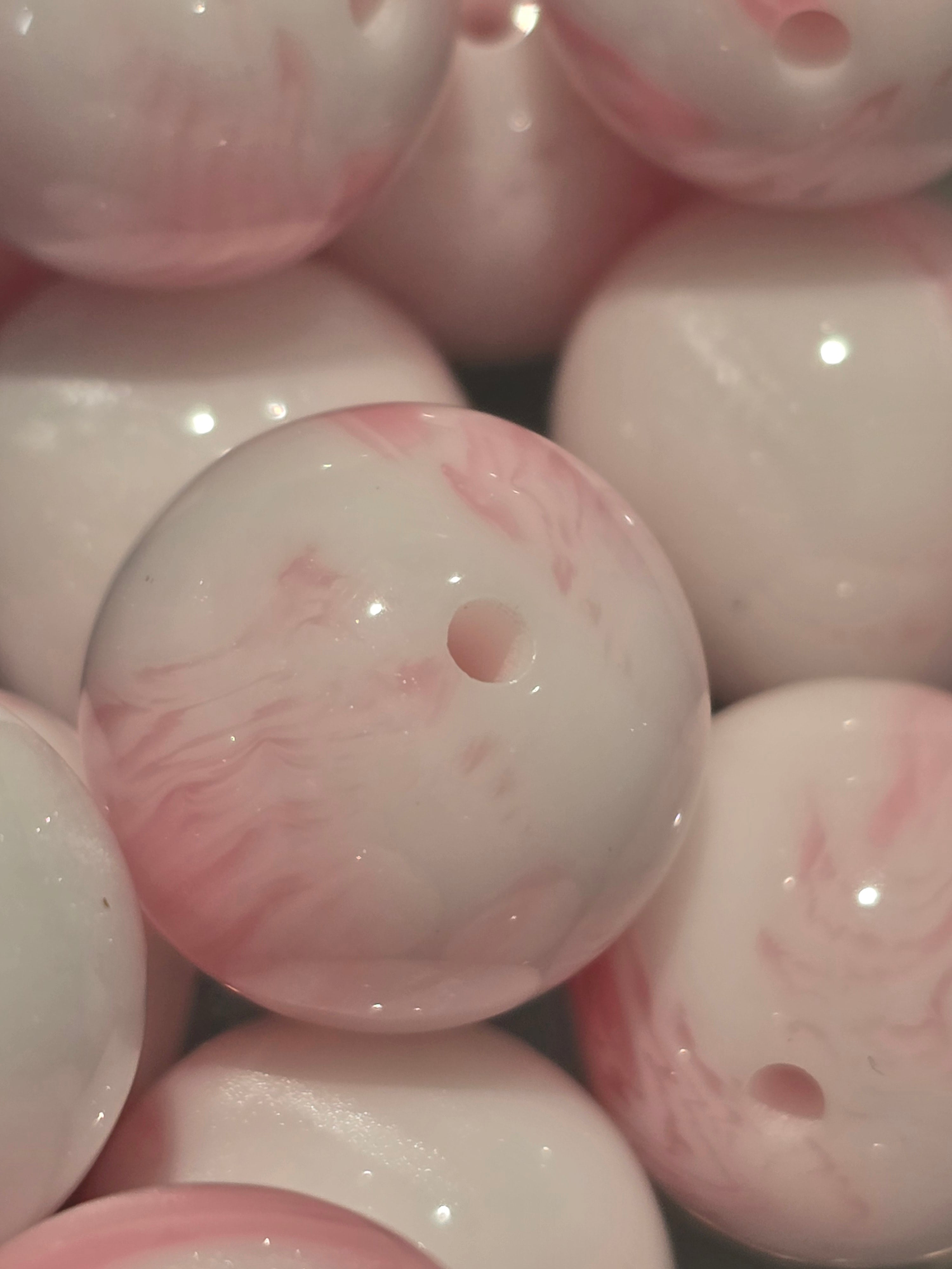 A close-up of glossy round beads with a white base and soft pink marbled swirls.