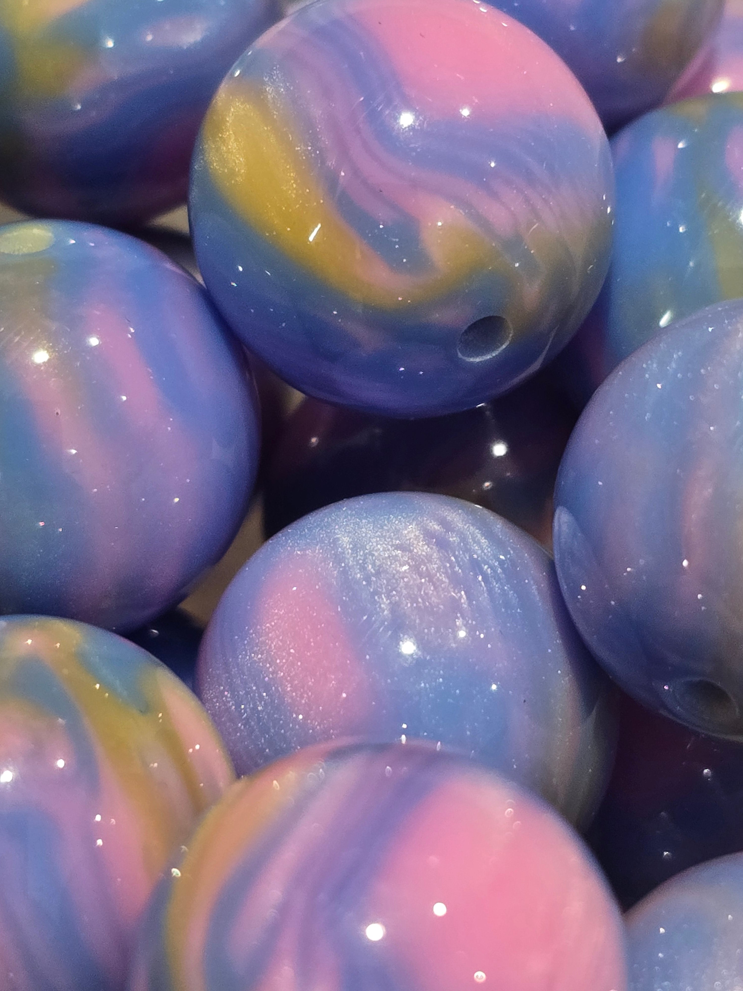 A close-up of glossy marbled beads in pastel purple, pink, blue, and yellow swirls with a glitter finish.