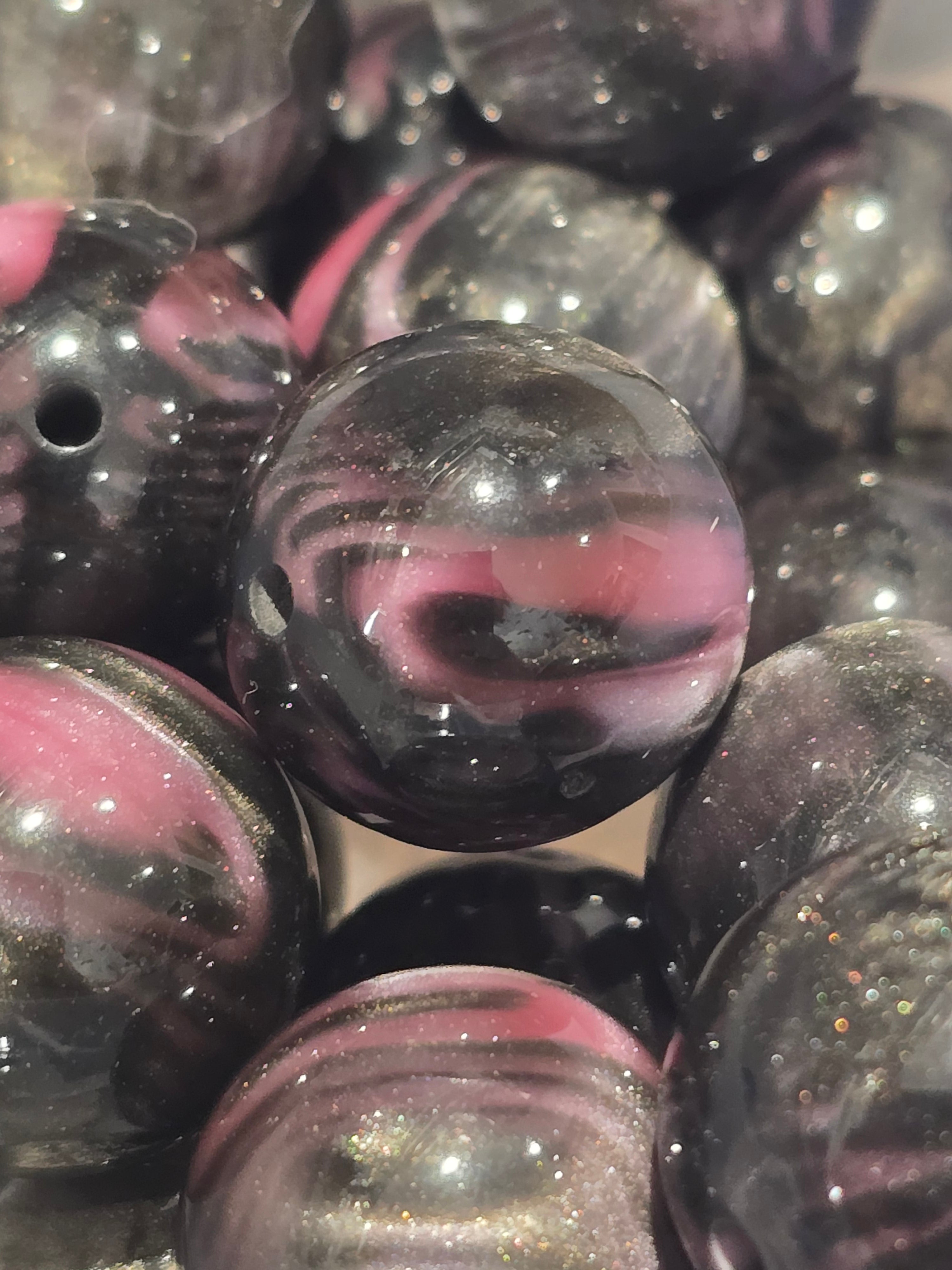 Close-up of glossy round craft beads with a marbled swirl pattern of black, pink.