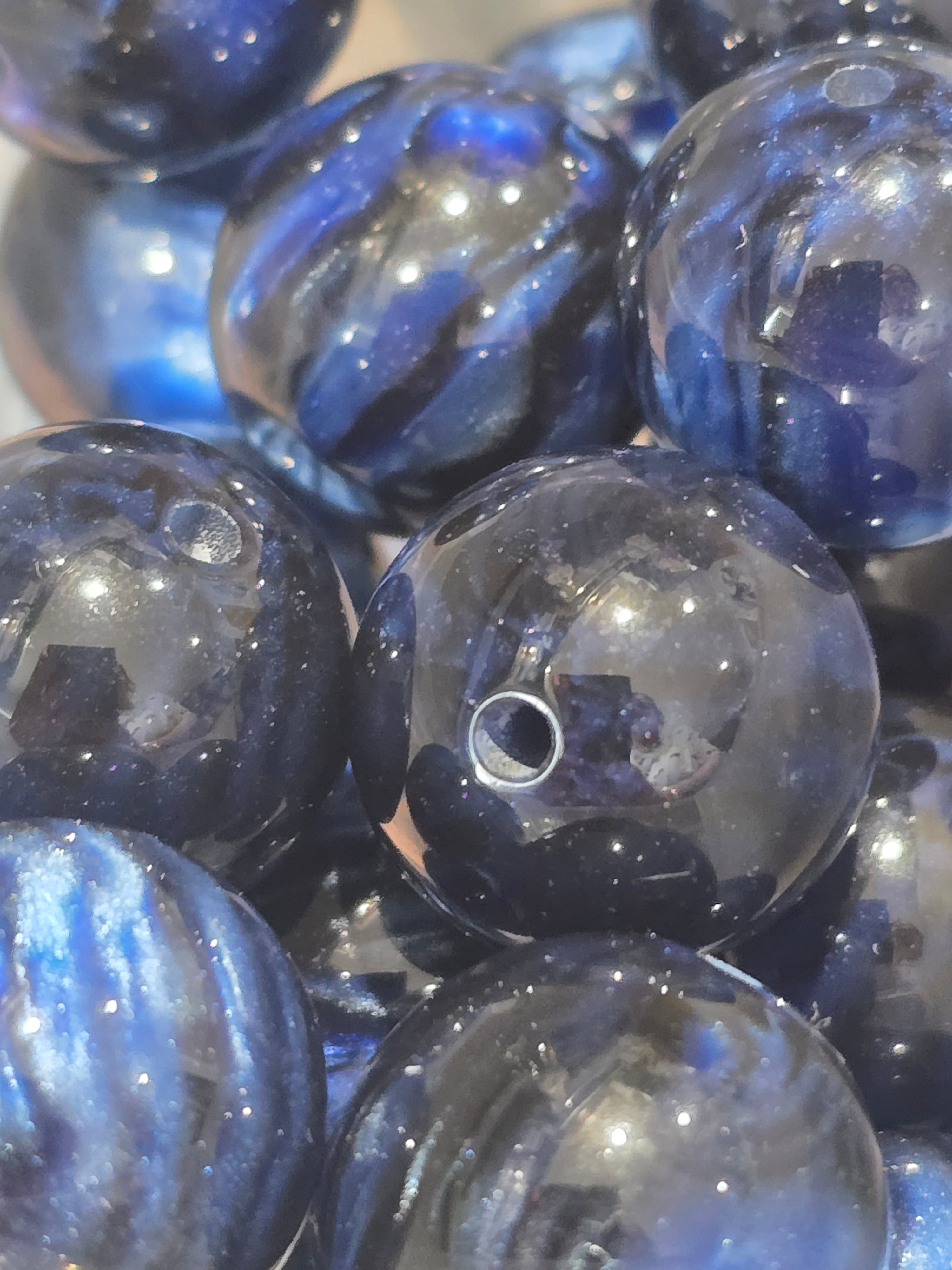 A close-up of glossy, round glass beads with a deep blue and black marbled pattern and subtle glitter.