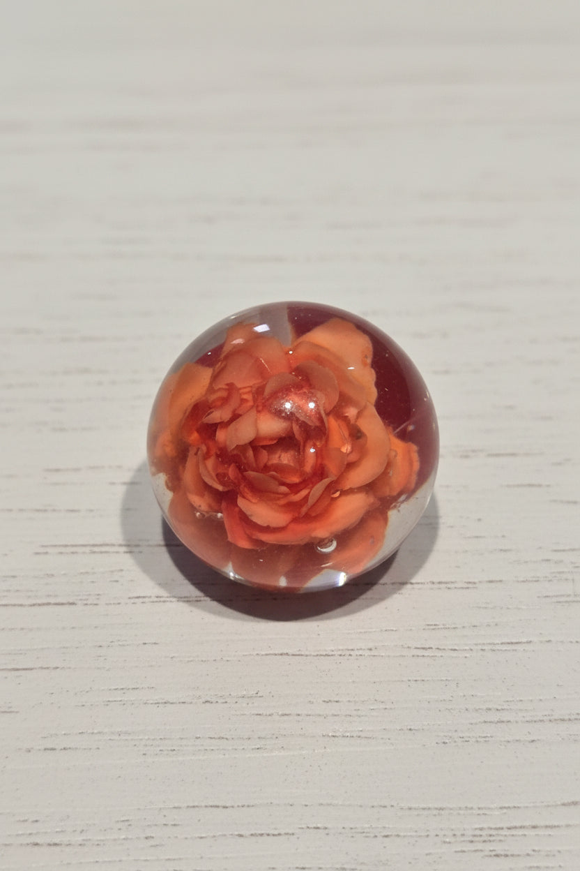 A clear glass top hole bead containing a detailed orange rose.