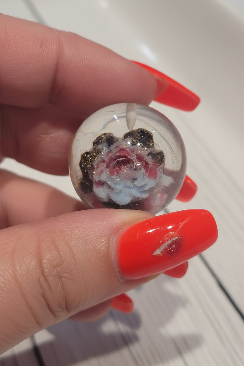 A resin bead pendant with a rose design in red, white, and black, with gold glitter inside.