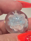 A clear round resin bead containing a light blue and white rose design.
