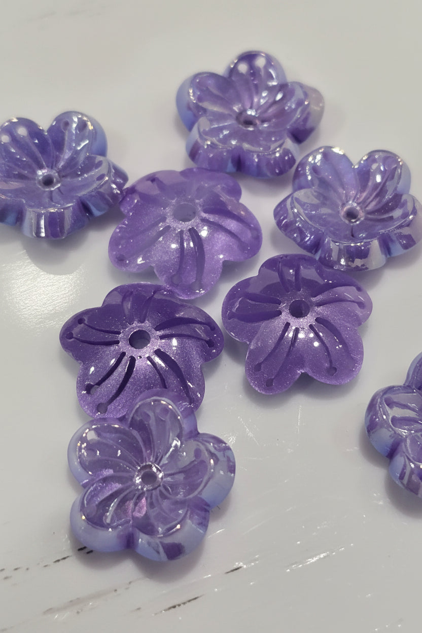 Translucent lavender-purple flower-shaped beads with a glittery finish scattered on a plain white surface.